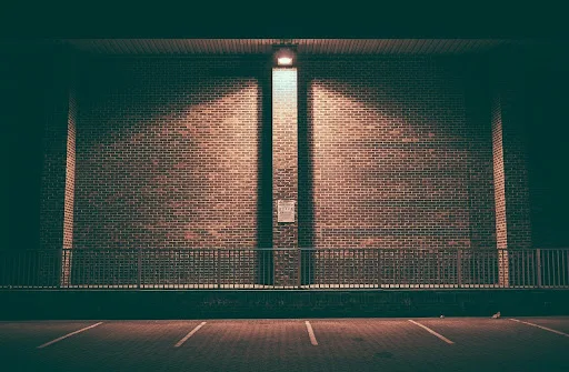A brick wall behind a railing is illuminated by a light.