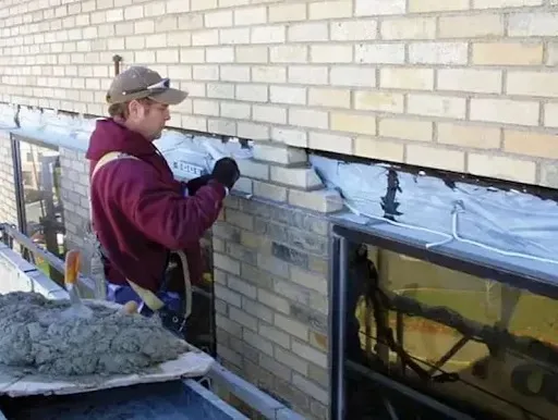 A masonry contractor repairs a section of brick wall with flashing and new bricks.