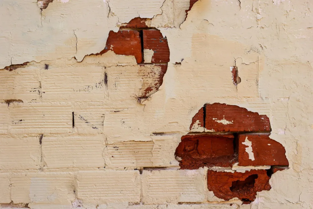 A white- painted brick wall shows evidence of mortar gaps, spalling bricks and structural damage.