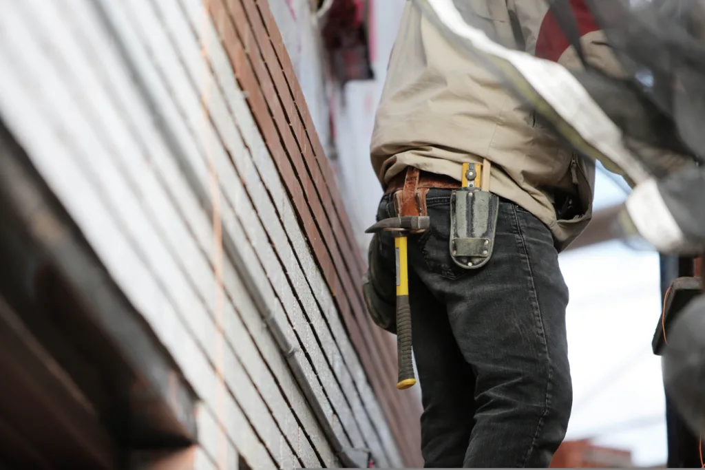 A construction worker in black jeans with tools hanging from his toolbelt.
